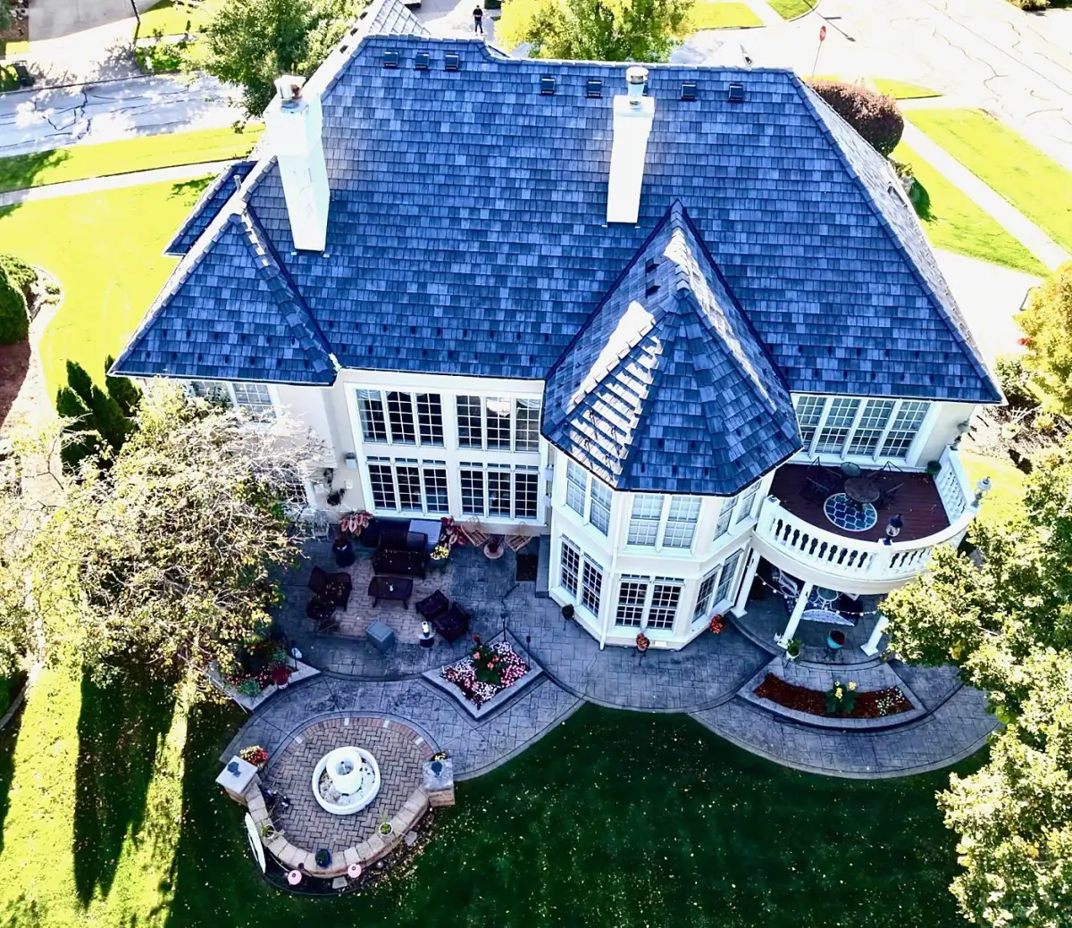 Aerial view of a cream two-story home with a blue-gray composite shake roof and turret
