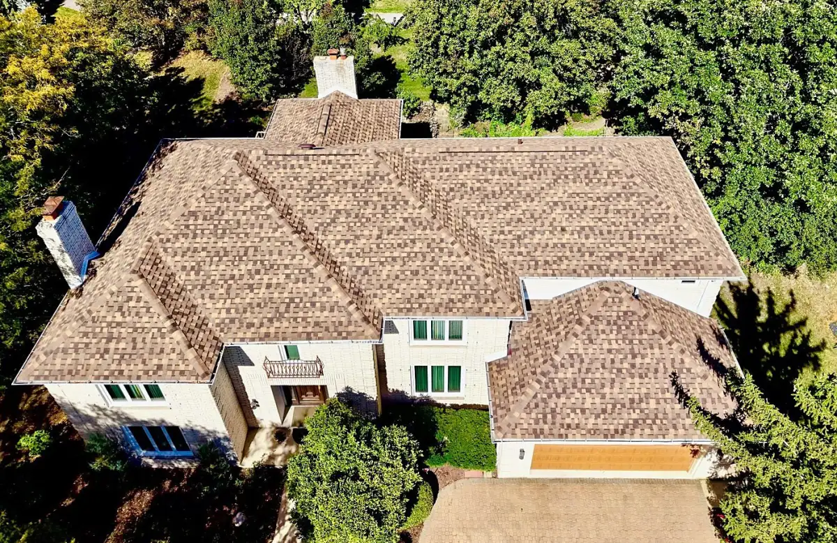 Aerial view of a cream brick home with a brown-blend architectural shingle roof
